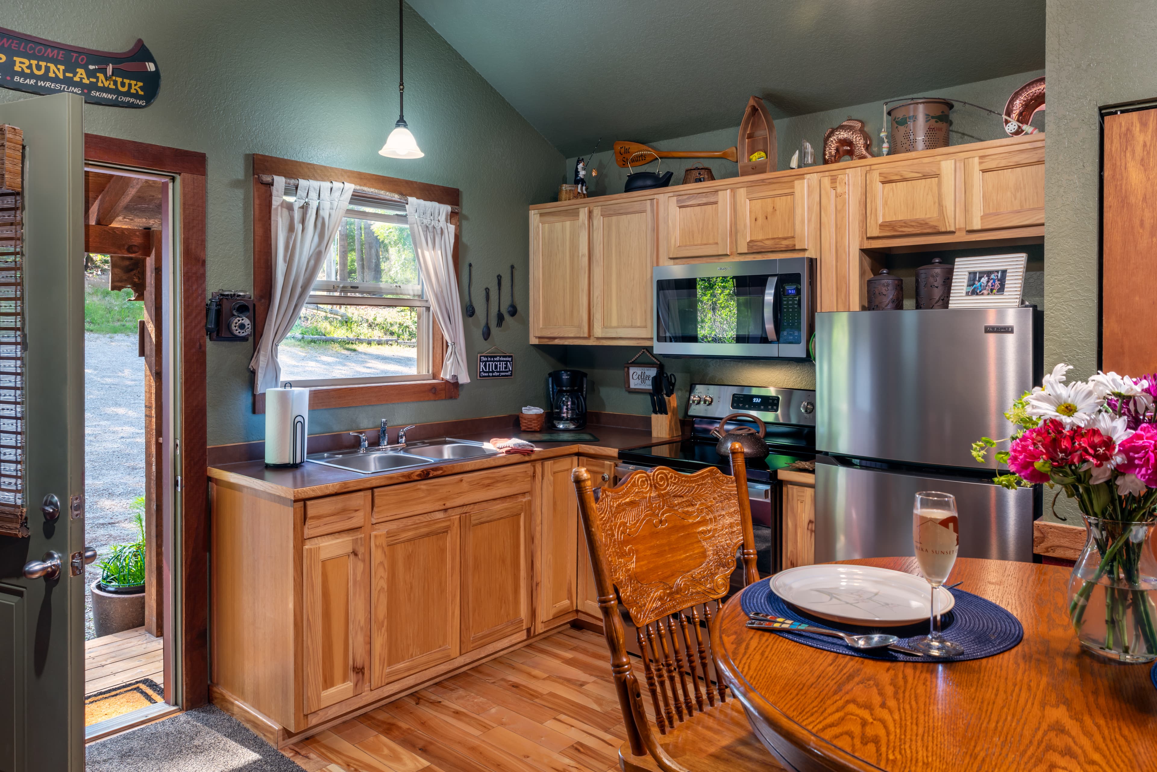 A cozy kitchen area in a rustic cabin featuring light wood cabinetry, stainless steel appliances, and a small dining table set for two.