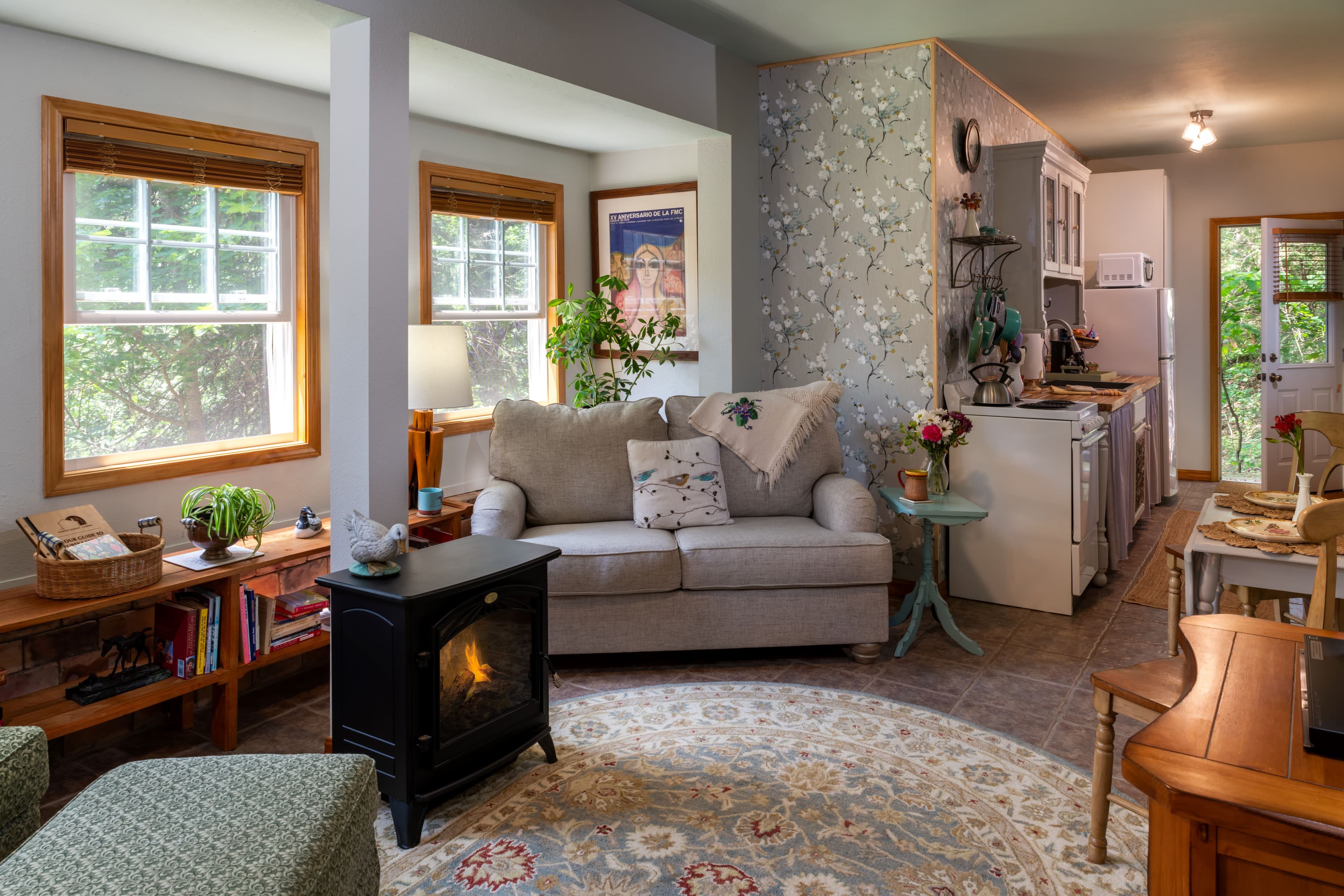 A cozy living room area featuring a light grey loveseat, a black electric stove with a warm glow, and a decorative round rug on the floor.
