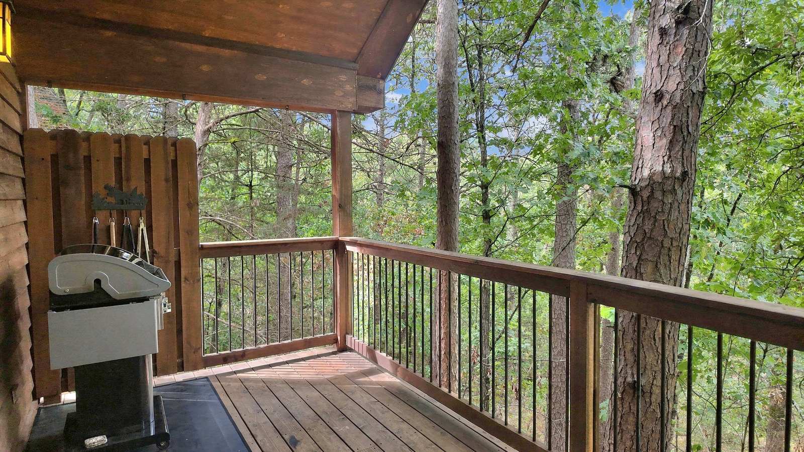 A wooden deck surrounded by trees features a grill and railing.