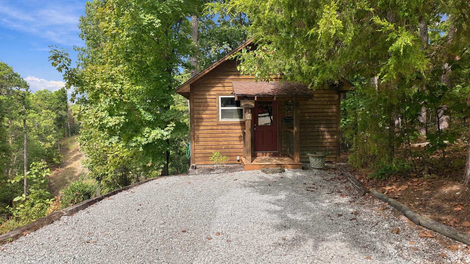A small wooden cabin surrounded by greenery on a gravel path.