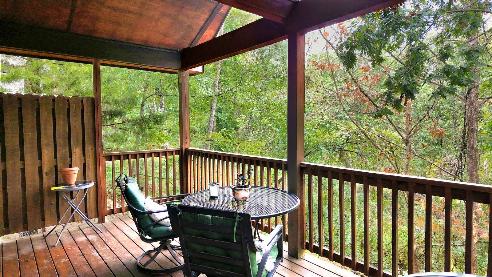 A cozy deck with a table and chairs, surrounded by lush greenery.