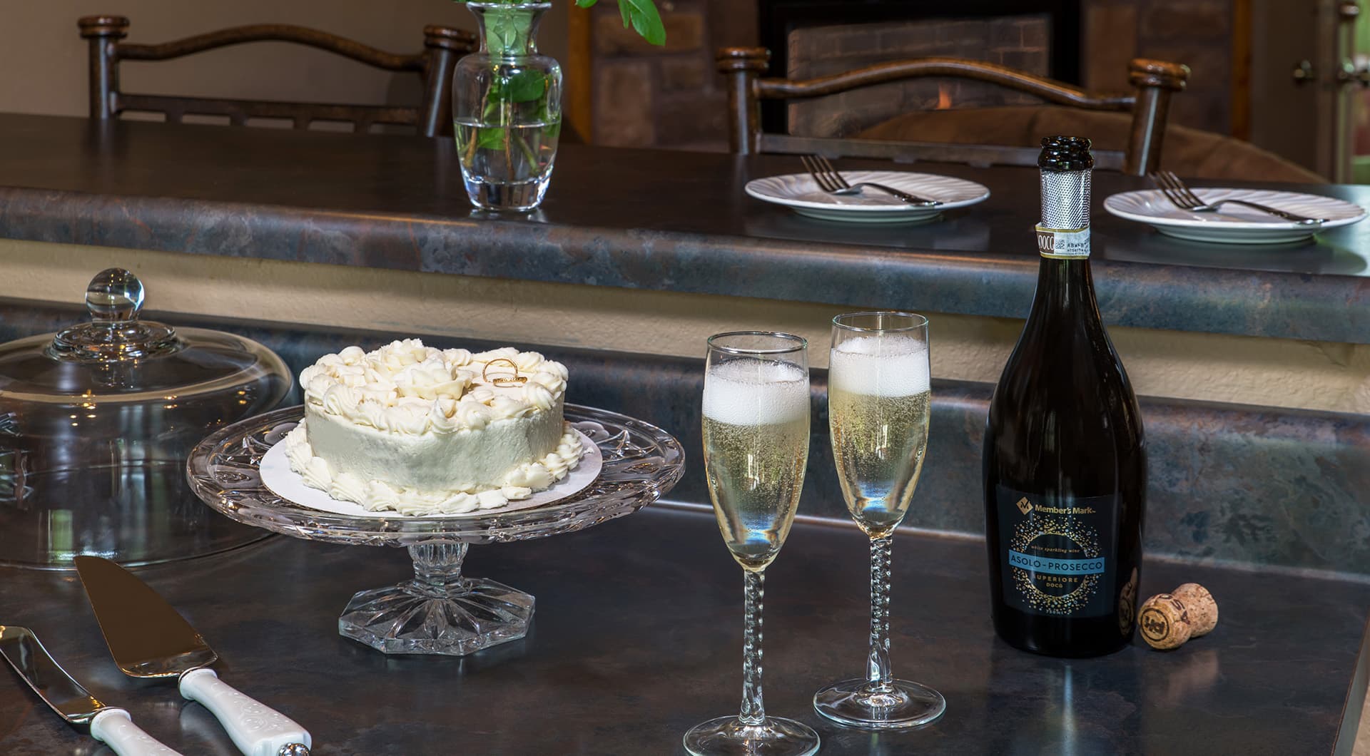 A elegantly set table featuring a cake, two flutes of champagne, and a bottle of sparkling wine.