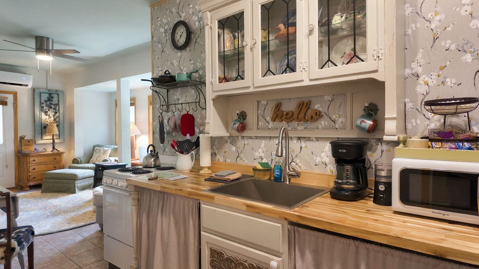 A cozy kitchen featuring wooden countertops, a sink, and appliances, with an adjoining living area visible in the background.